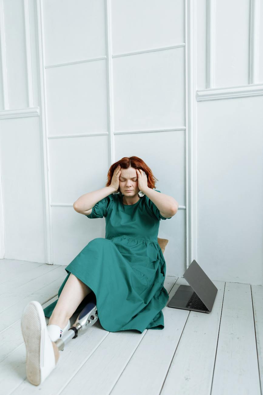 a stressed woman touching her head while sitting on the wooden floor
